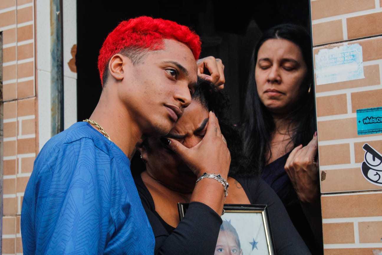 Esta foto captura um momento intenso de emoção e apoio entre três pessoas. O jovem artista Oruam de cabelo vermelho conforta uma mulher que segura uma moldura com a foto de um menino. Essa é a mãe do Herus, que chora por conta da morte do seu filho. Esse registro aconteceu no Santo Amaro. Foto: Uendell Vinicius